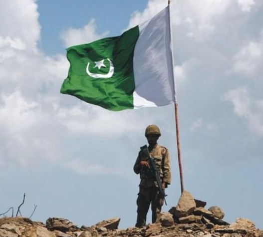 Pakistan Flag Lovers - A Pakistani soldier with a large Pakistani Flag - Proud Display of Pakistani flag Proud Display of Pakistani Flag - A Pakistani soldier with a rifle and helmet standing under a large Pakistani Flag - Pakistani Flag Lovers