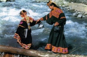 Photos of Kalash Women; A Kalash woman and her daughter wearing Traditional black dress - Pictures of Kalash Women, Kalash Valleys, Chitral Pictures of Kalash Women: A Kalash woman helping her daughter cross a stream - Photos of Kalash Valleys of Chitral